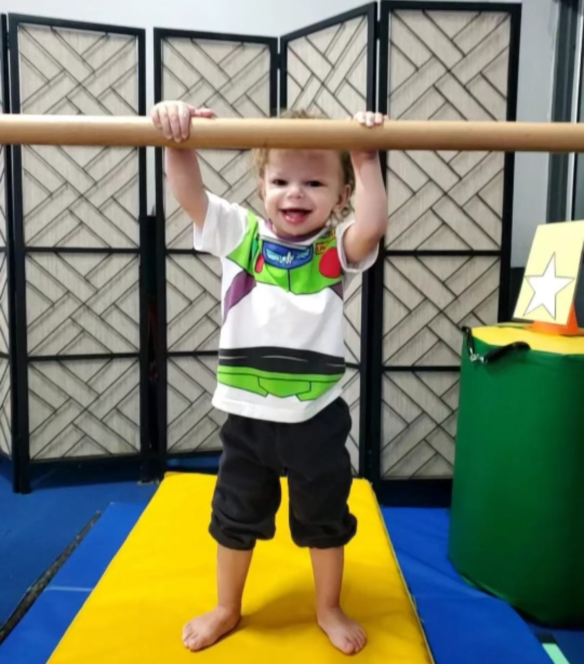 A little boy wearing a buzz lightyear shirt is hanging from a bar