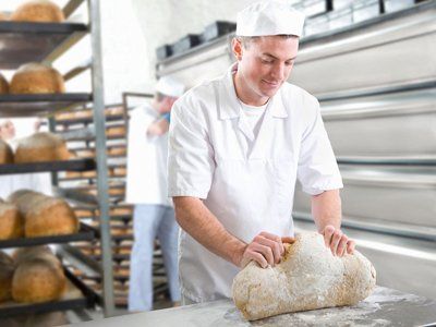 A baker at work, kneading dough in front of shelves of cooked bread