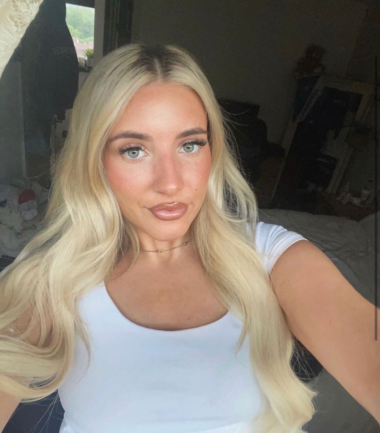 A blonde woman in a white shirt is taking a selfie.