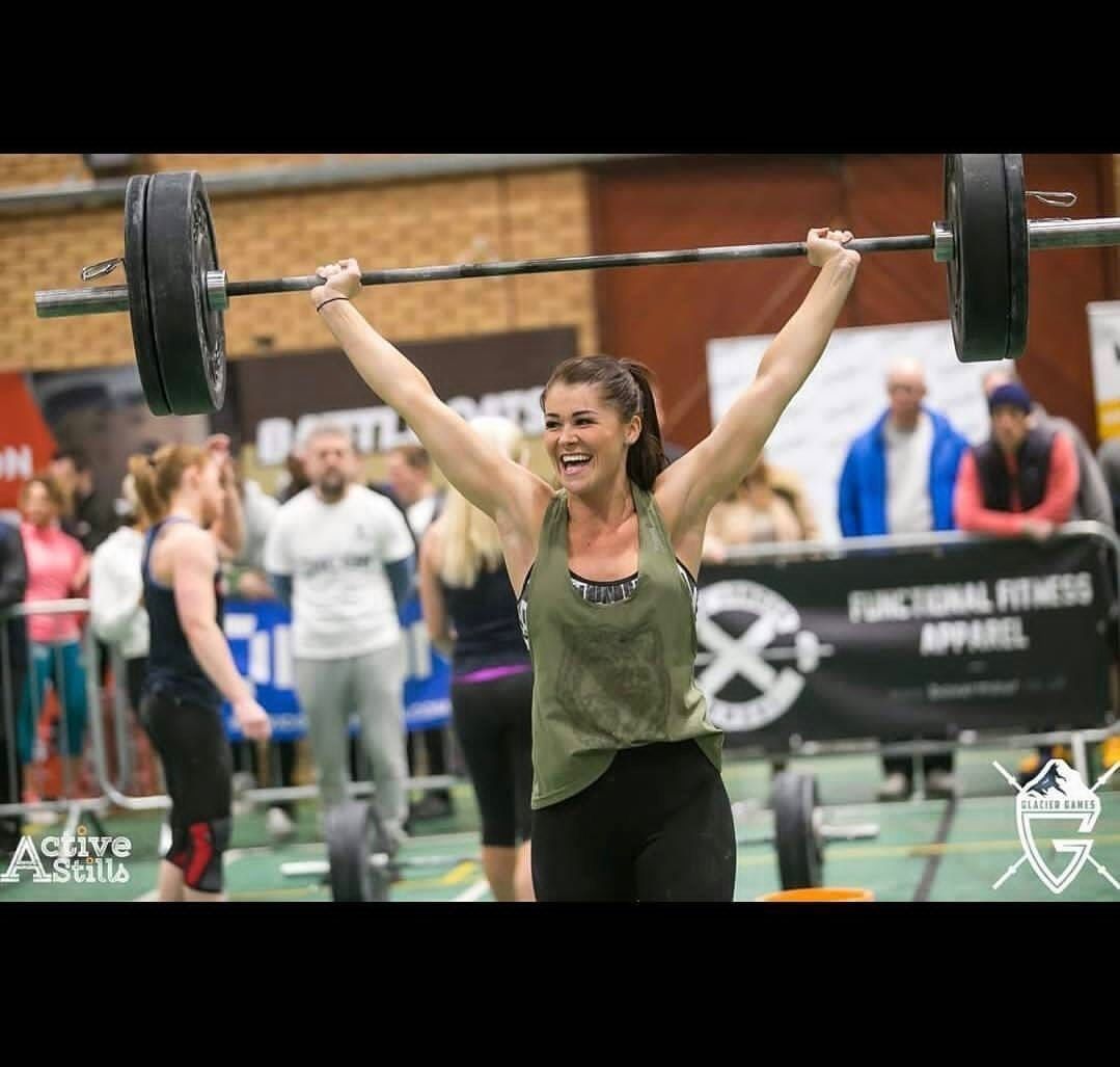 A woman is lifting a barbell over her head in a gym.