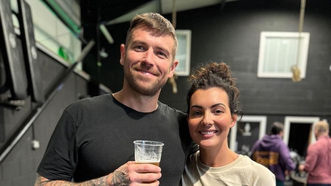 A man and a woman are standing next to each other holding a glass of beer.