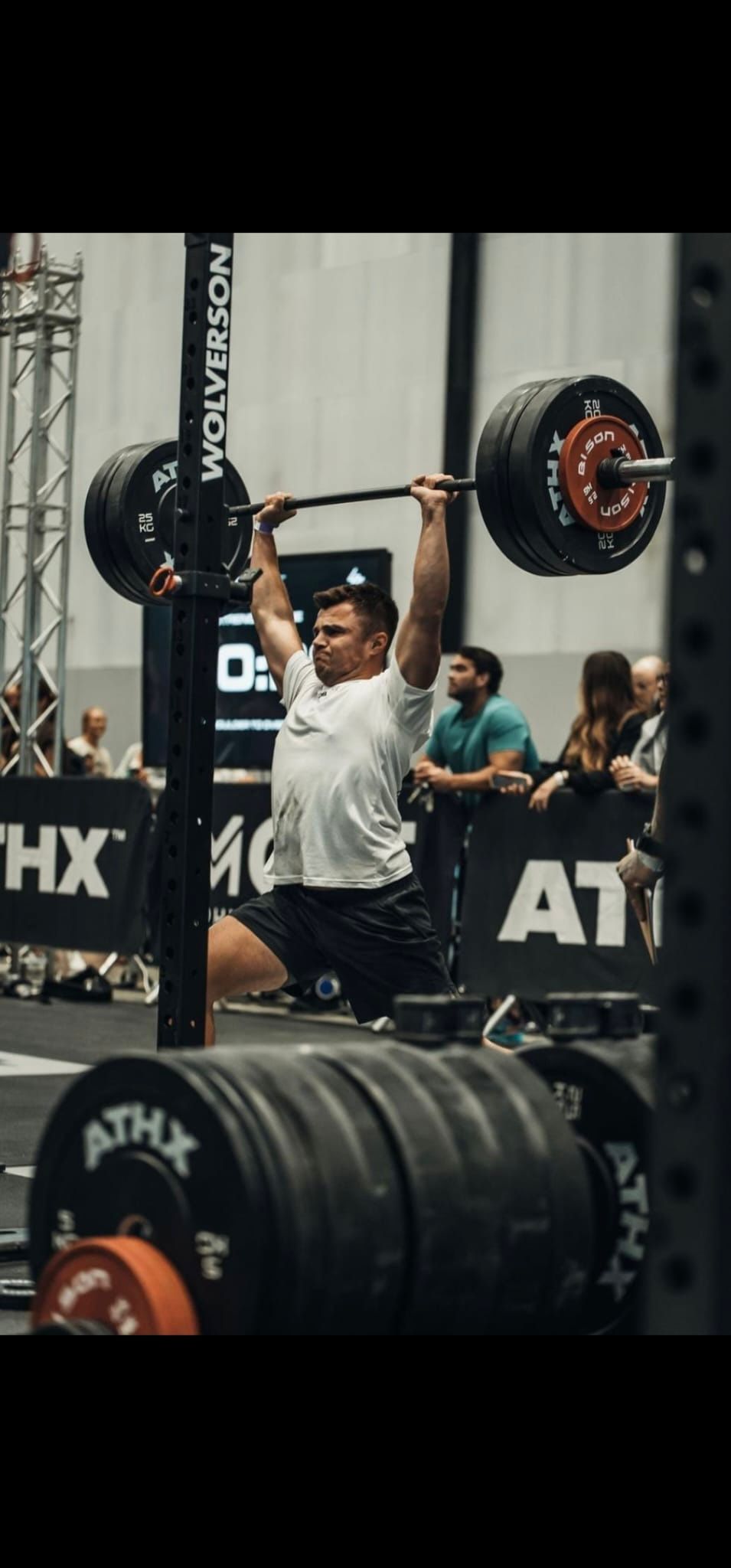 A man is lifting a barbell over his head in a gym.