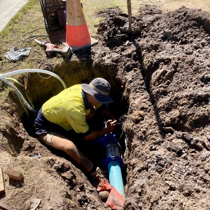 A Man in a Yellow Shirt is Working on a Pipe in the Dirt — Shawline Plumbing and Drainage In Iluka, NSW