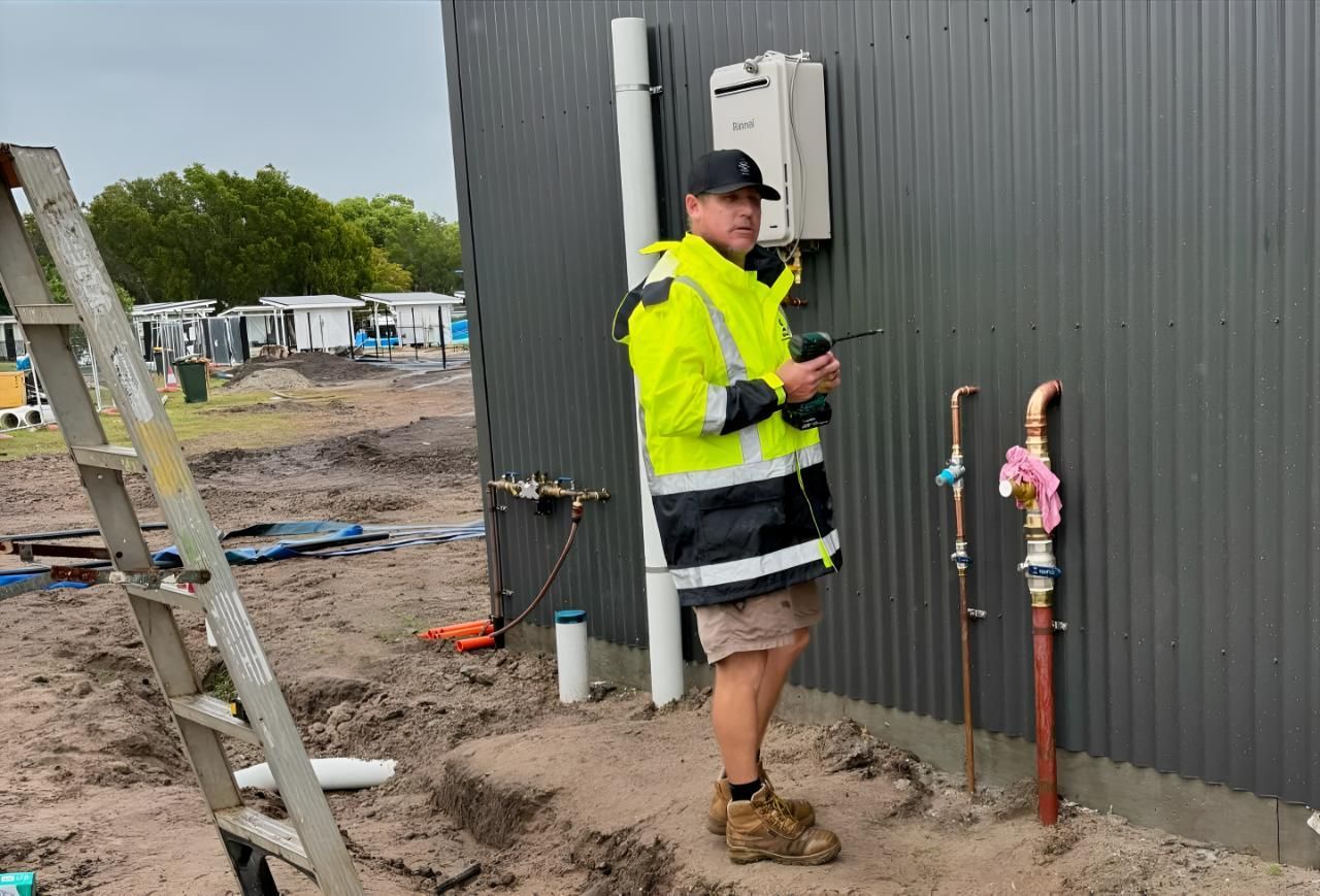 A Man in a Yellow Jacket is Standing in Front of a Building — Shawline Plumbing and Drainage In Iluka, NSW