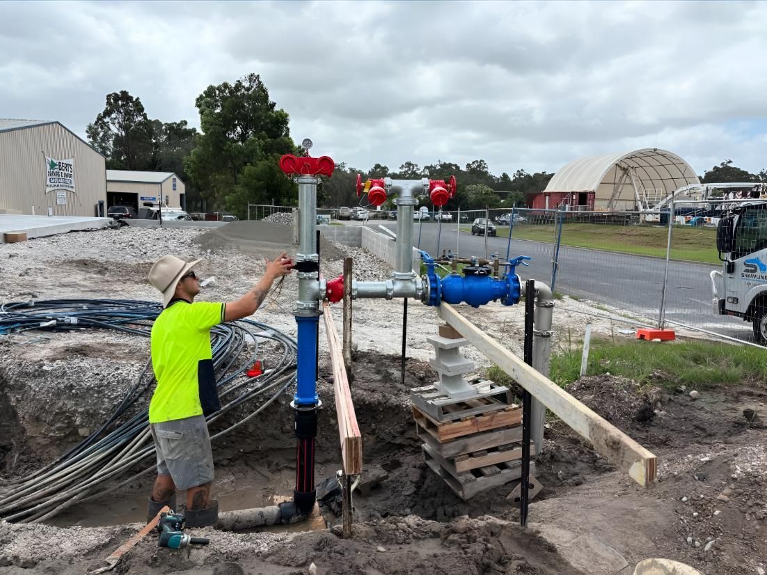 A Man in a Yellow Shirt is Working on a Pipe in the Dirt — Shawline Plumbing and Drainage In Iluka, NSW