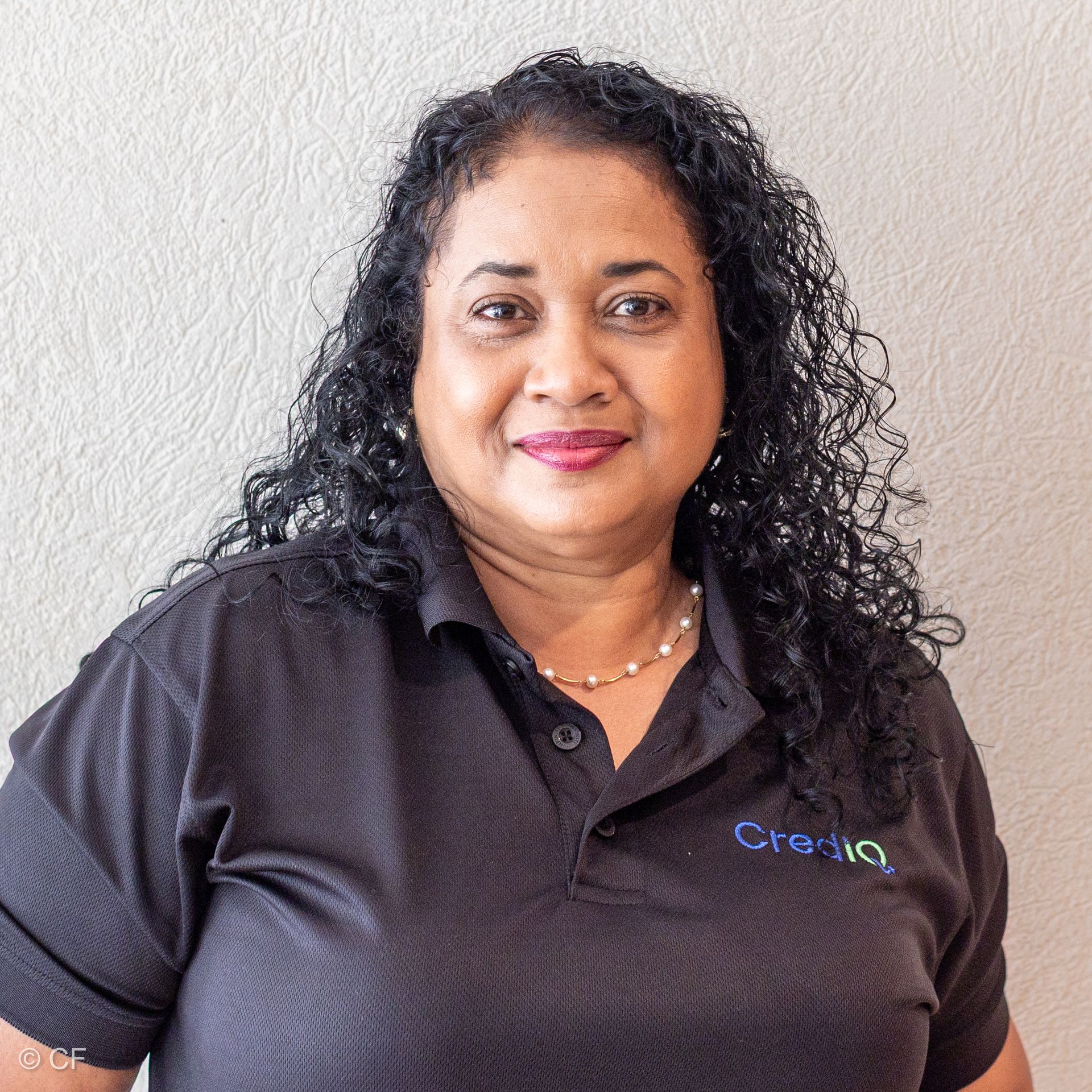 Cassian Gyan smiling wearing a black polo shirt with a company logo, against a light wall.