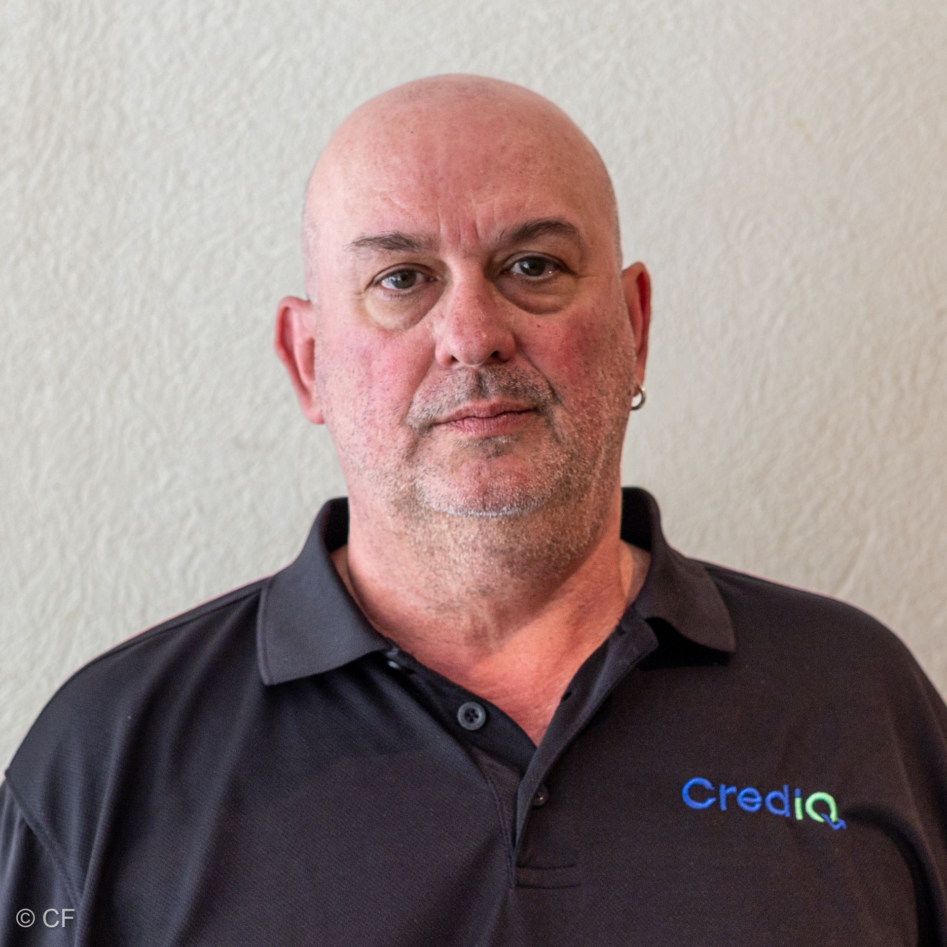 Clive Fletcher wearing a grey polo shirt with a Crediq logo against a plain, textured off-white wall.