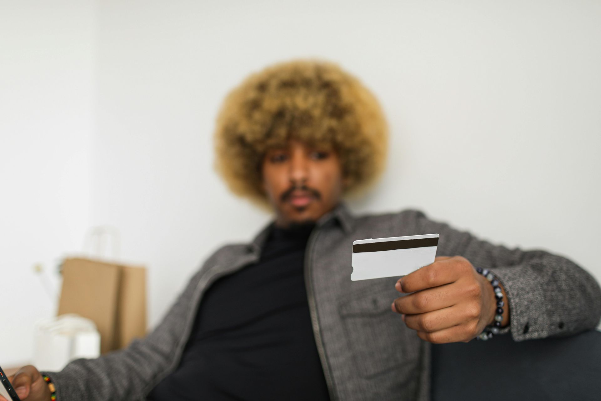 Man with afro holds a credit card, blurred background.