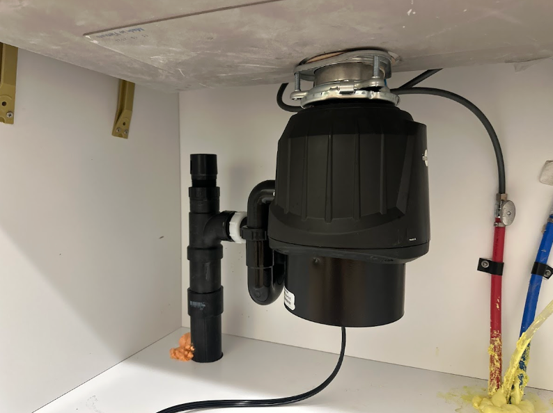 Under-sink garbage disposal with black drain pipes and red and blue water valves.