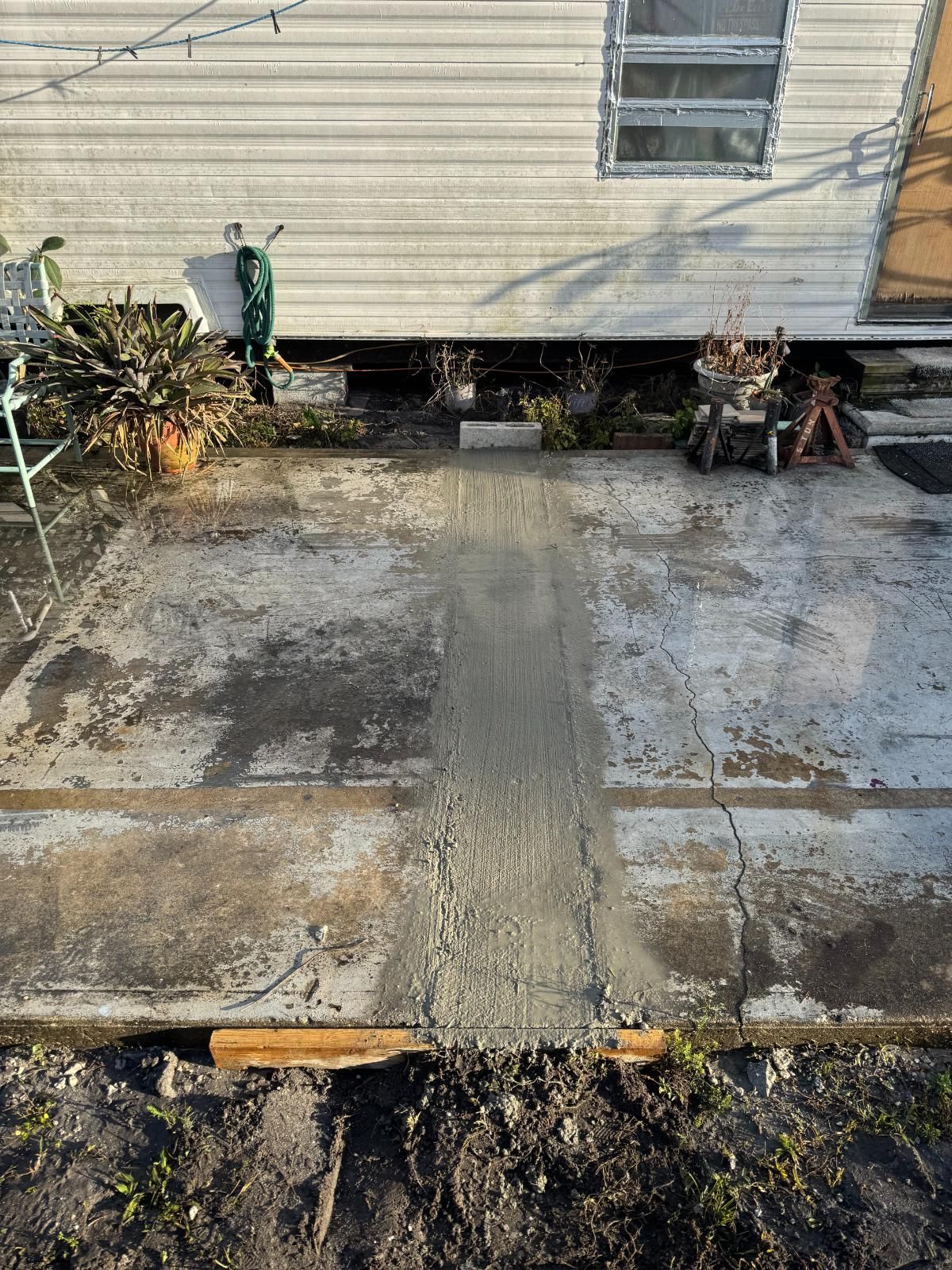 Concrete walkway leading to a beige building wall, with muddy ground and shrubs on both sides.