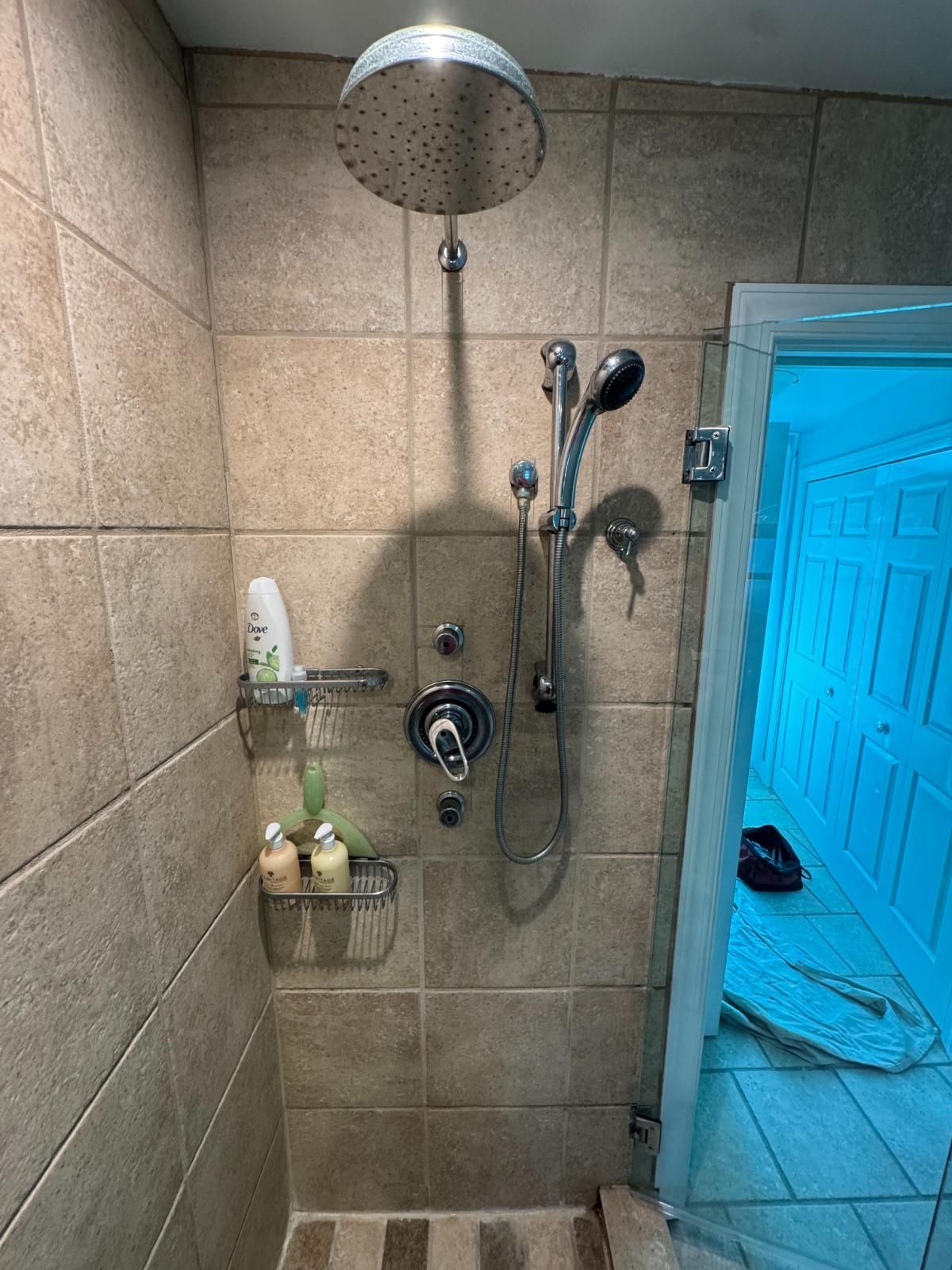 Bathroom shower with tiled walls, rainfall head, hand shower, and shelves with toiletries.
