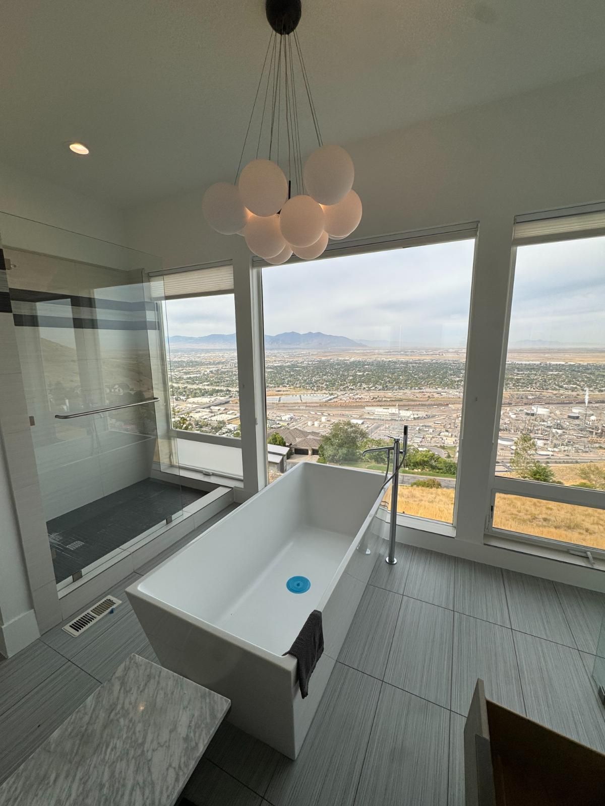 Modern bathroom with freestanding tub and floor-to-ceiling windows overlooking a city and mountains