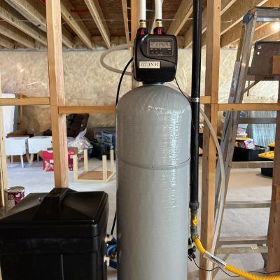 Silver water softener tank with digital control head in a basement utility area