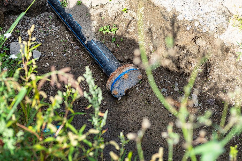 Black irrigation pipe with rusted connector lying in a dirt trench outdoors.