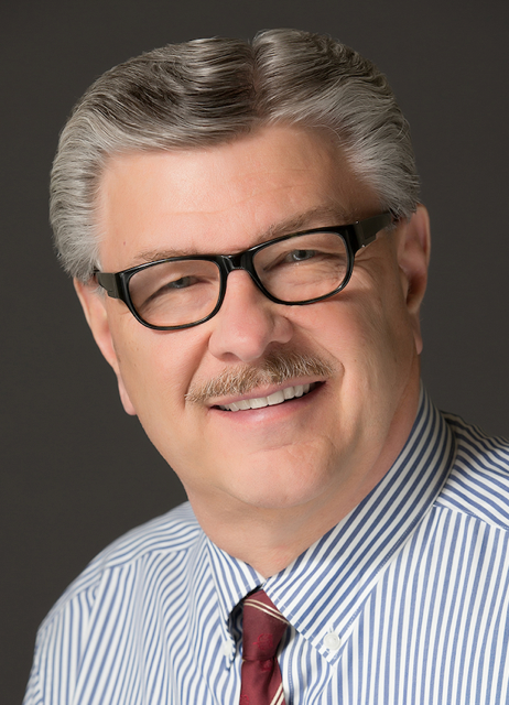 A man wearing glasses and a striped shirt is smiling for the camera.