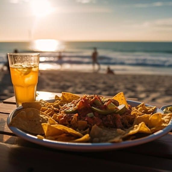 A plate of nachos and a glass of beer on a table on the beach.