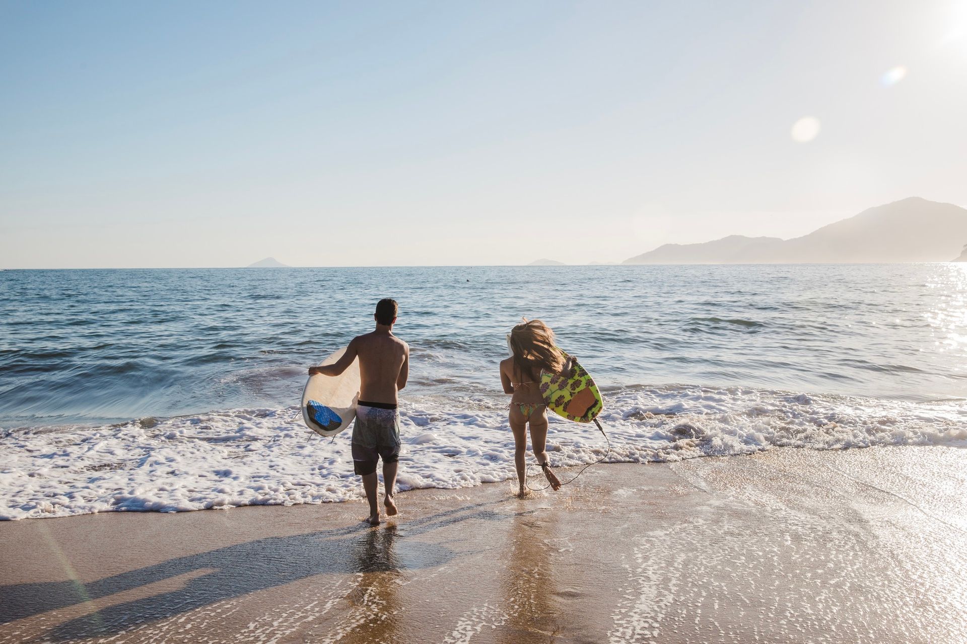 A man and a woman are walking on the beach carrying surfboards.