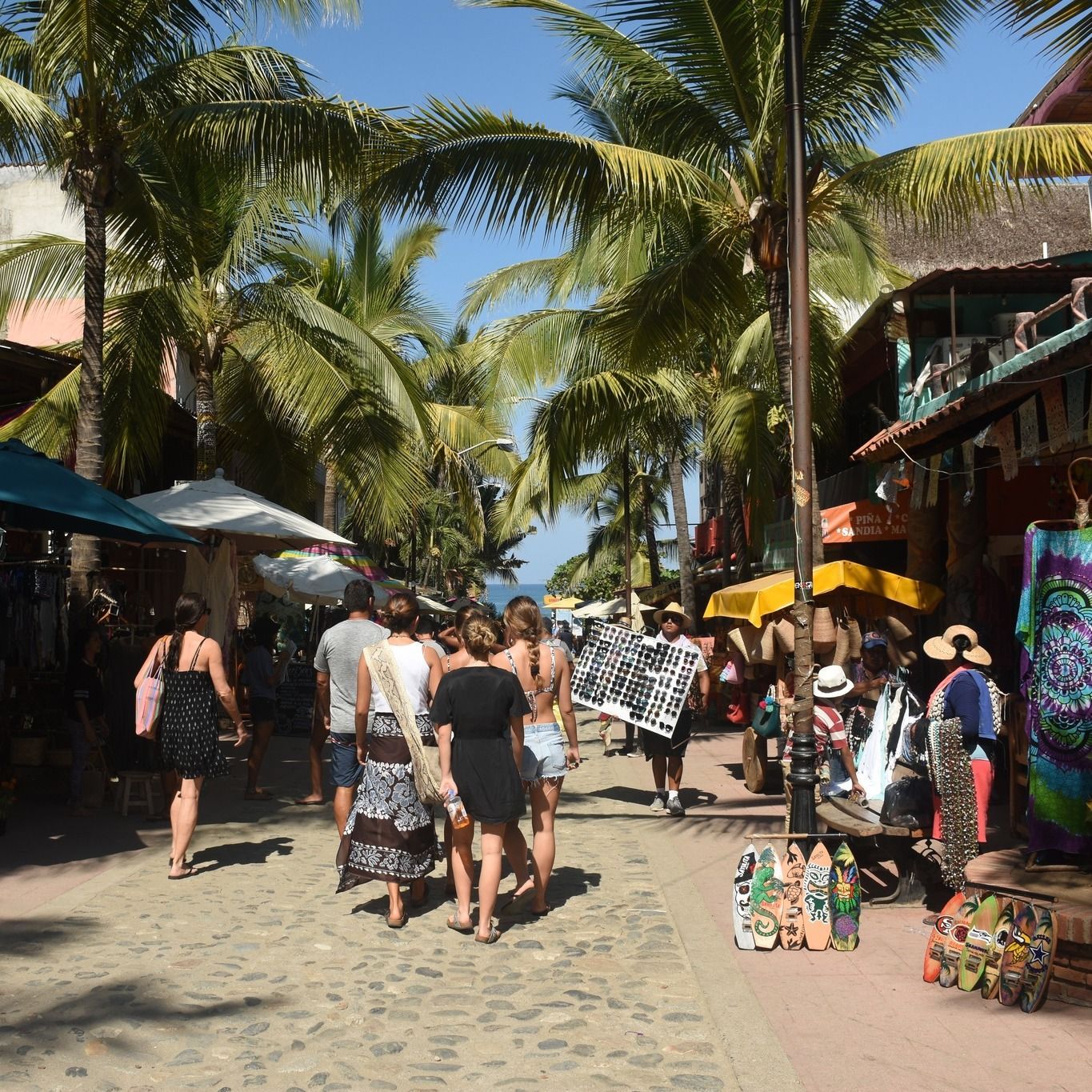 A group of people are walking down a street lined with palm trees