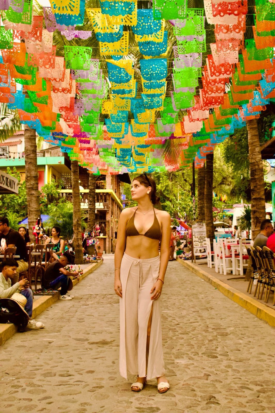 A woman in a bikini is standing under a canopy of colorful paper flags.