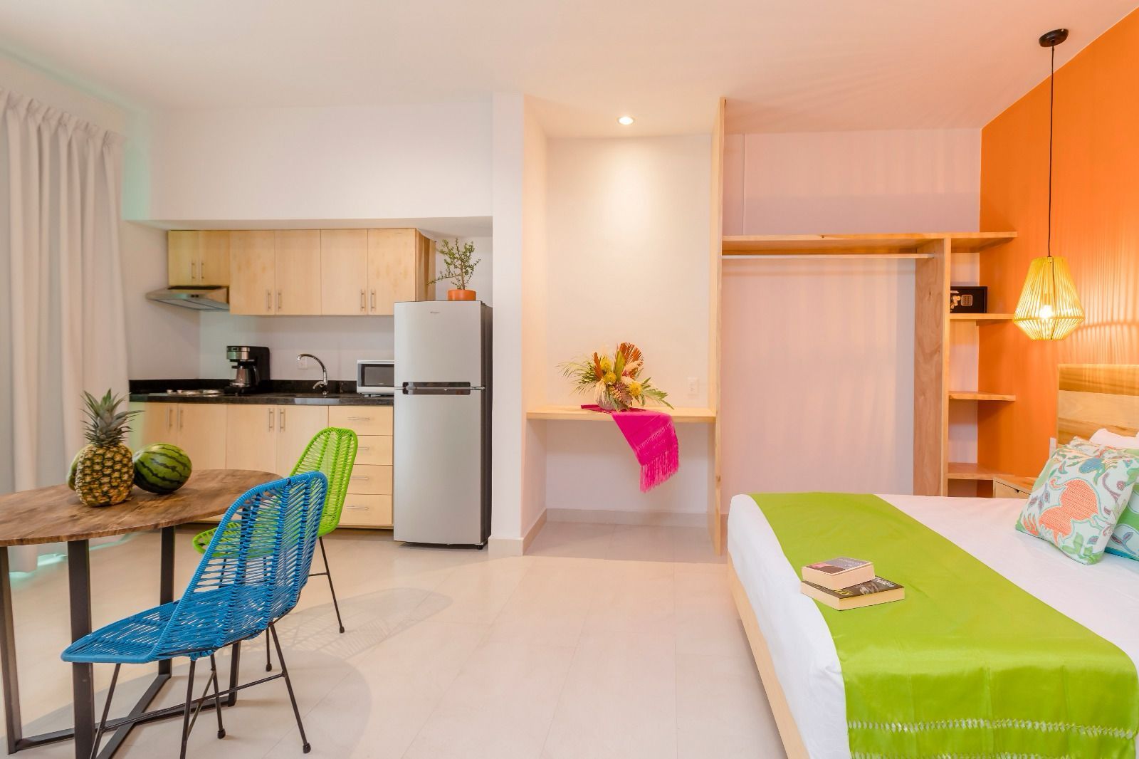 A hotel room with a bed , table , chairs and a refrigerator.