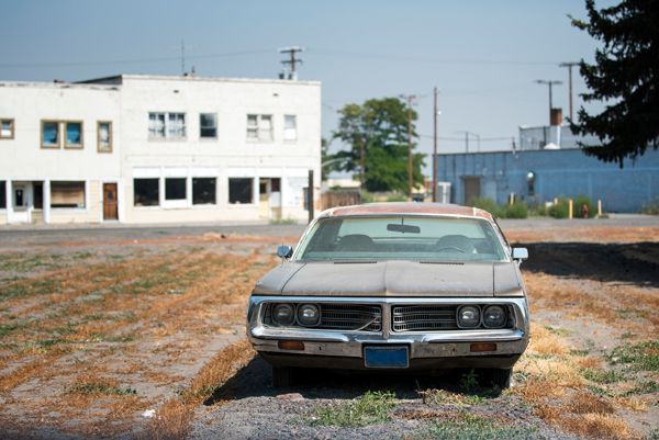 A picture of an abandoned car sitting in the middle of a village.