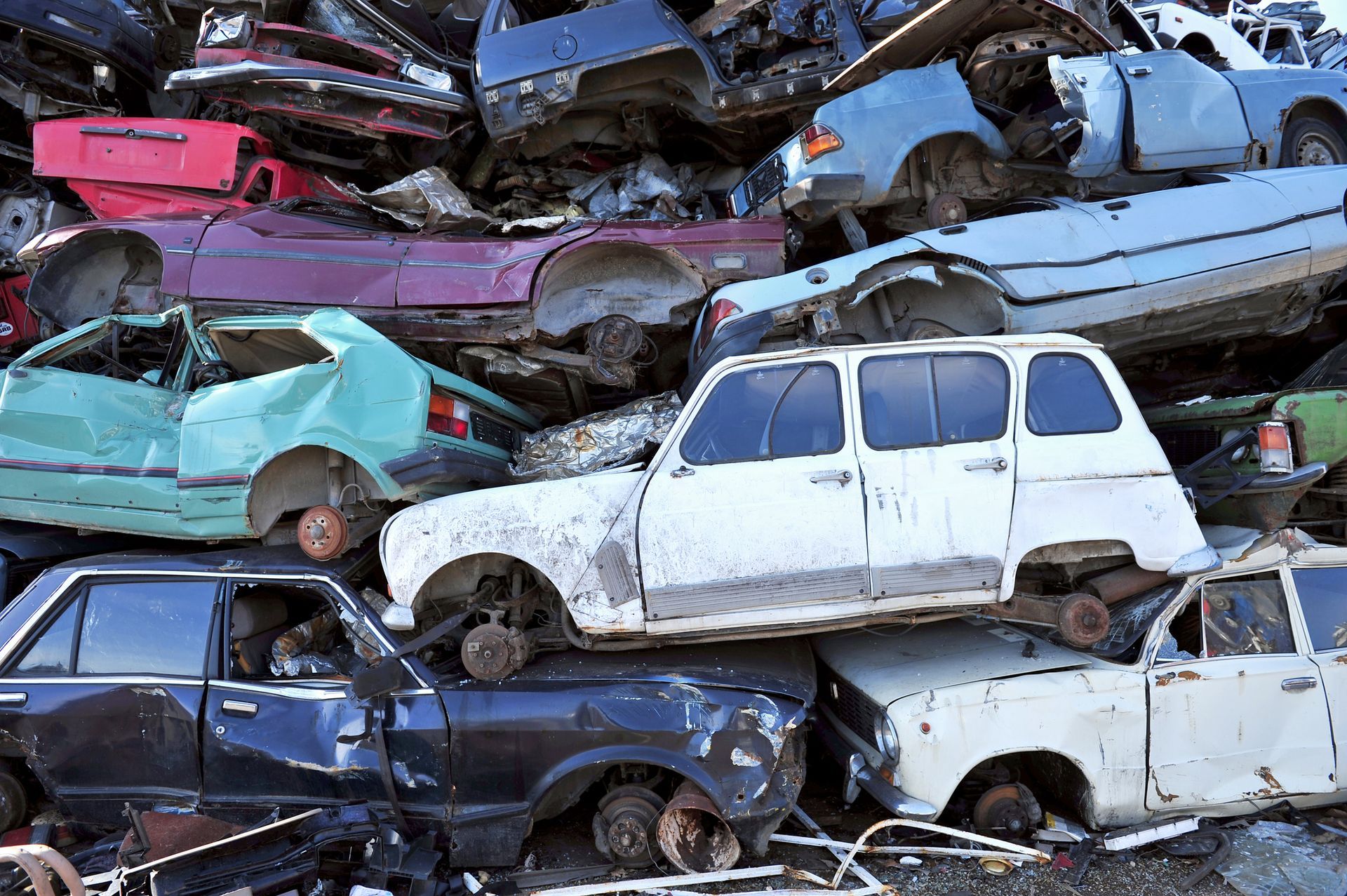 Pile of crushed and damaged cars at a junkyard, various colors and styles.