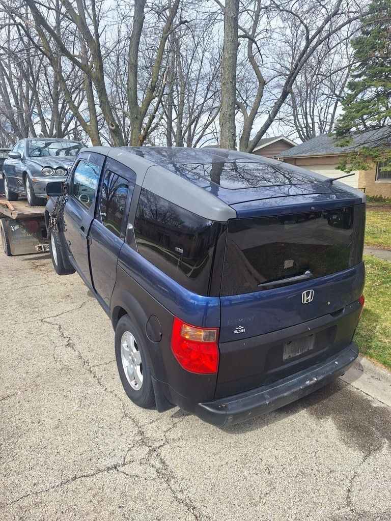 Blue and black Honda Element with extended roof on a trailer, parked on a street.