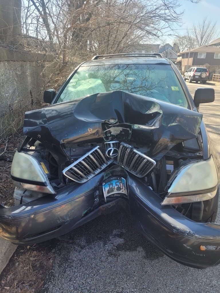 Black car with extensive front-end damage; hood crumpled, bumper detached; parked on street.