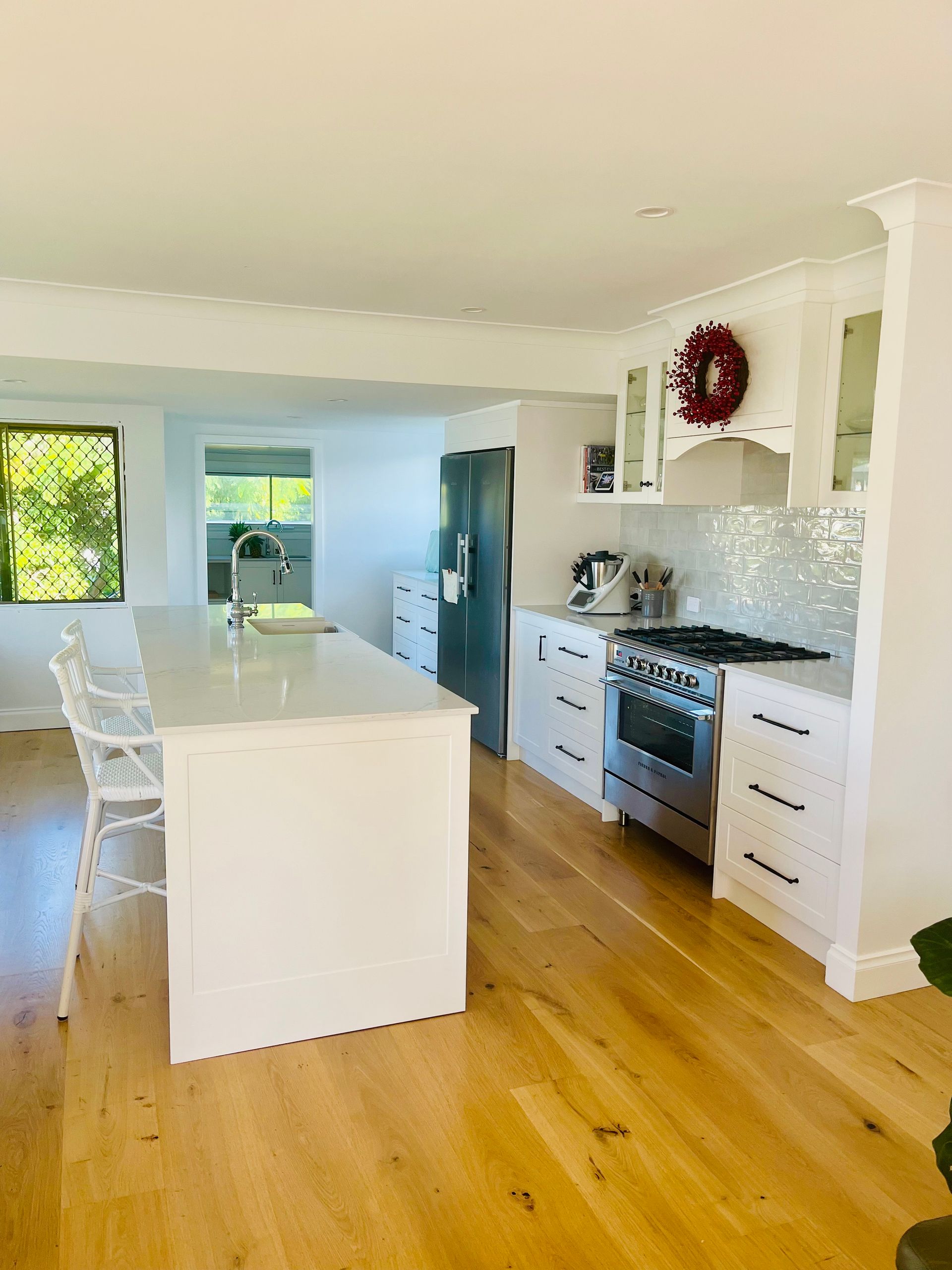 Bright, modern kitchen with white cabinets, island, stainless steel appliances, and wooden floors.