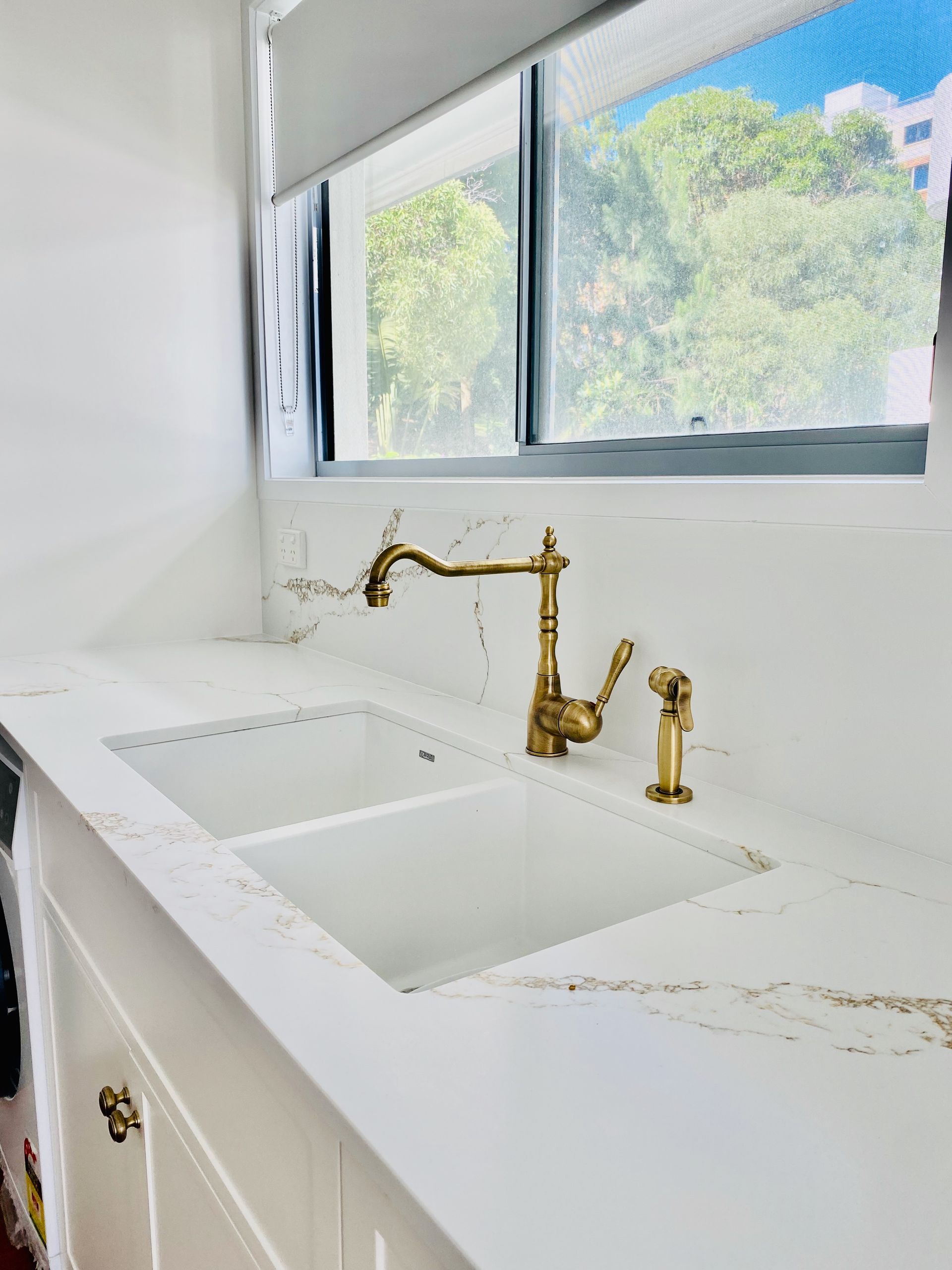 White kitchen sink with gold faucet near a window.