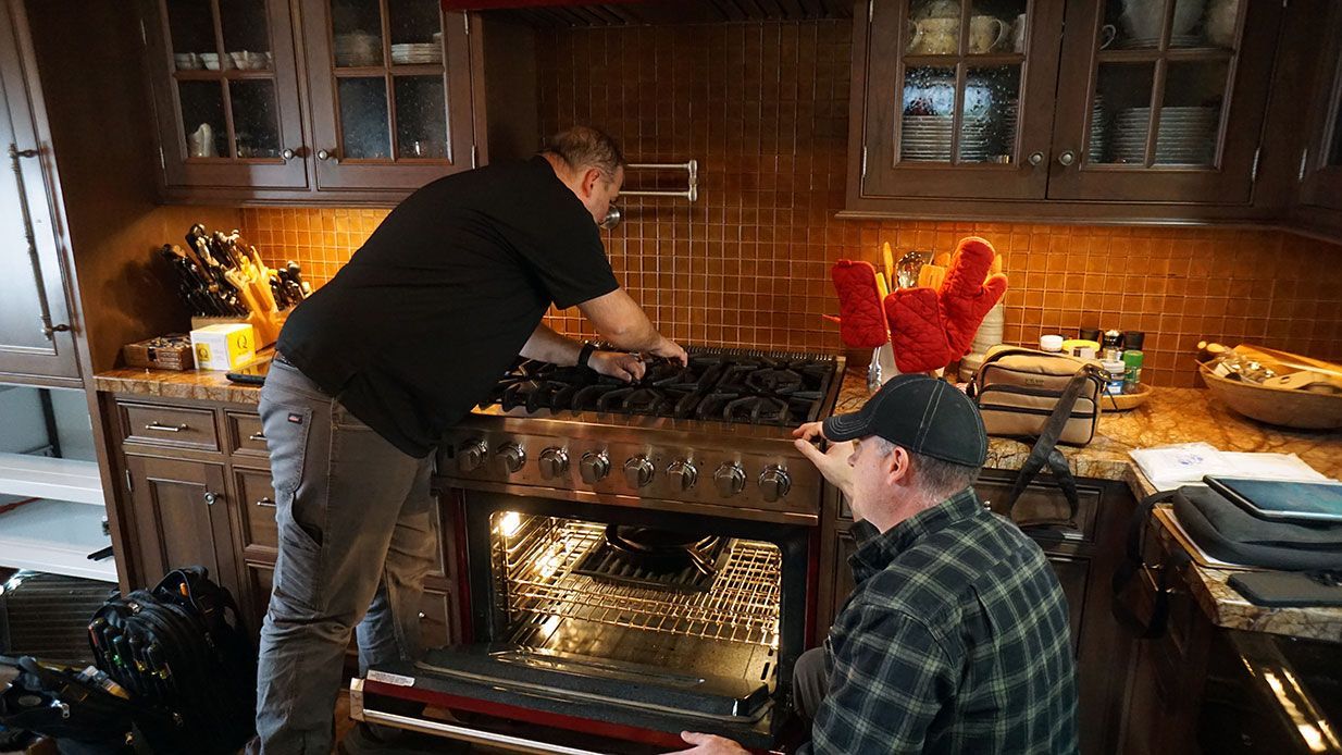 a team of technicians make an adjustment to a residential viking brand gas range