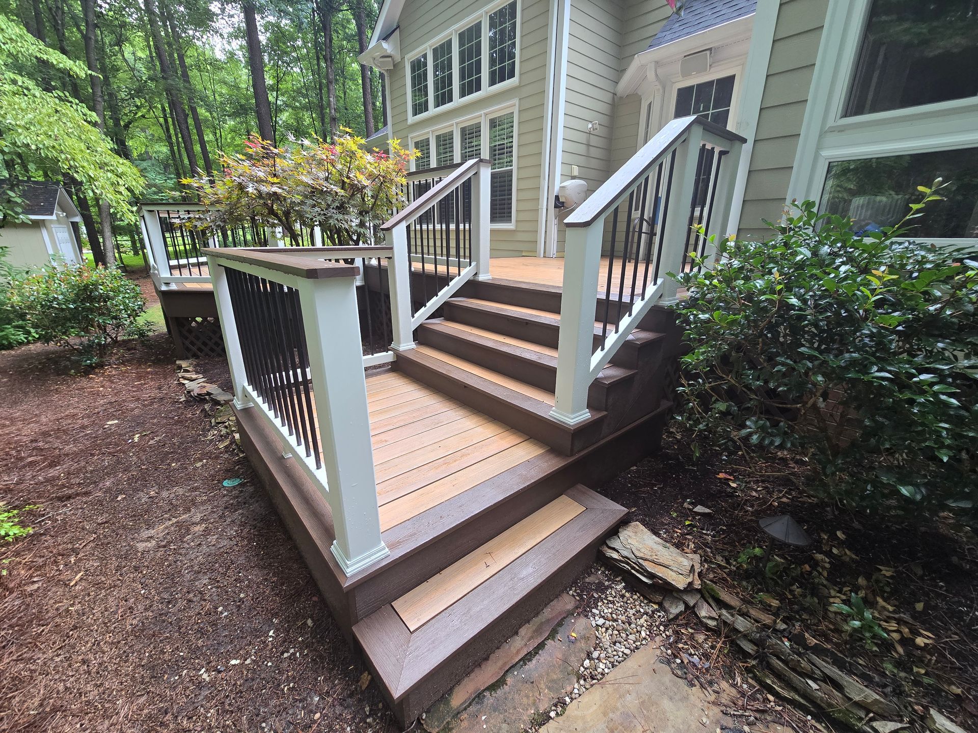 Wooden deck stairs with white railings and dark brown trim leading up to a residential house exterior.