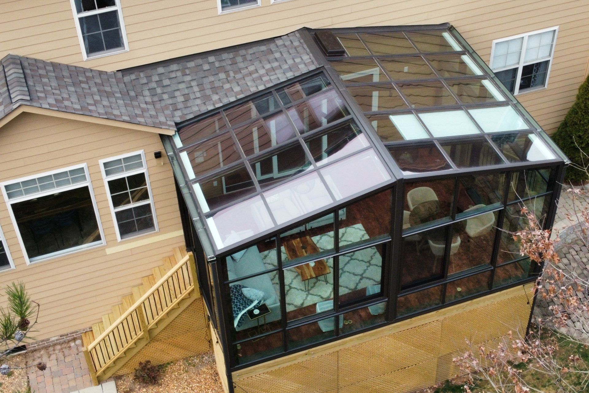 An elevated view of a sunroom with a glass roof attached to the rear of a beige, two-story suburban home.