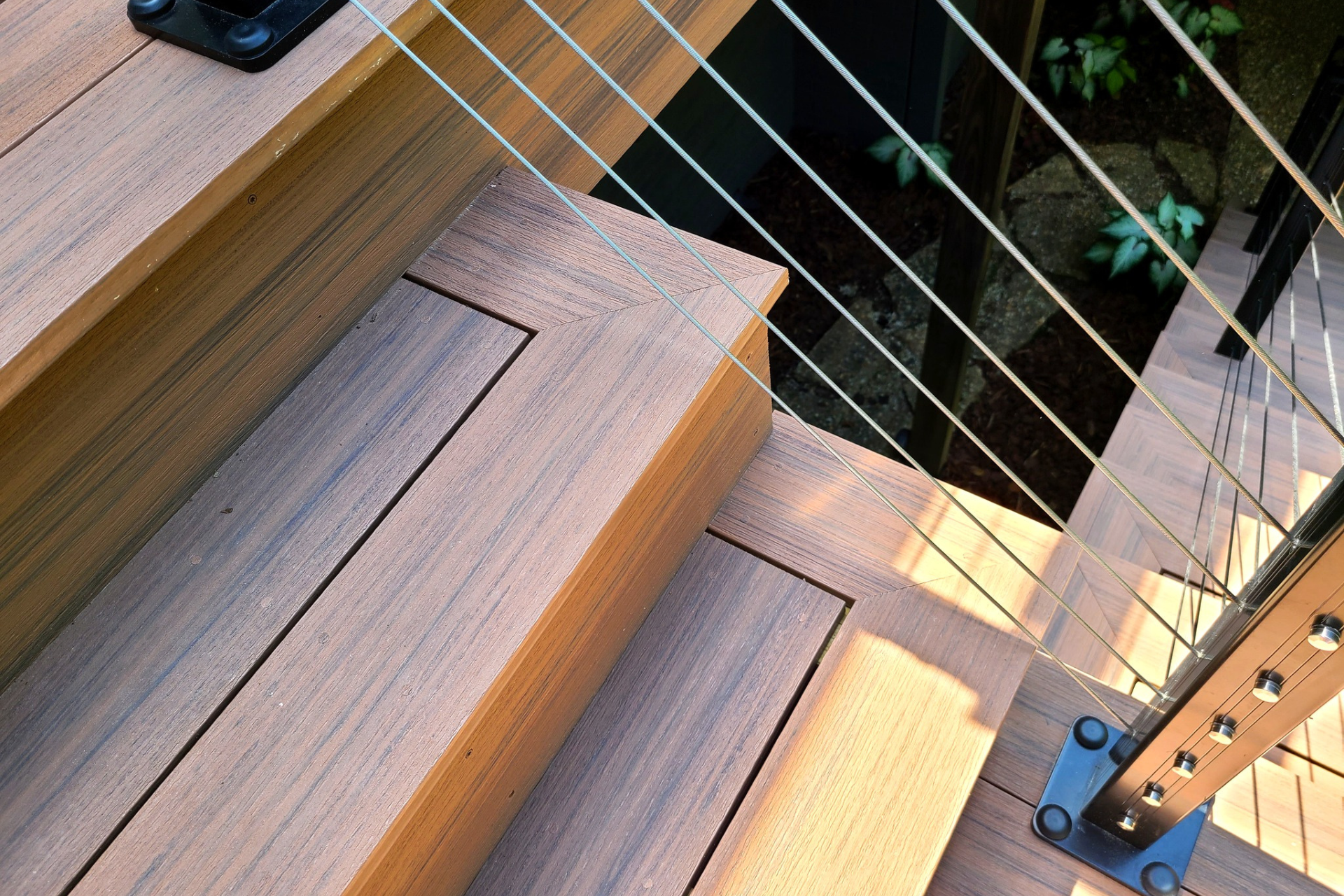Close-up of wooden deck stairs featuring a dark metal cable railing system.