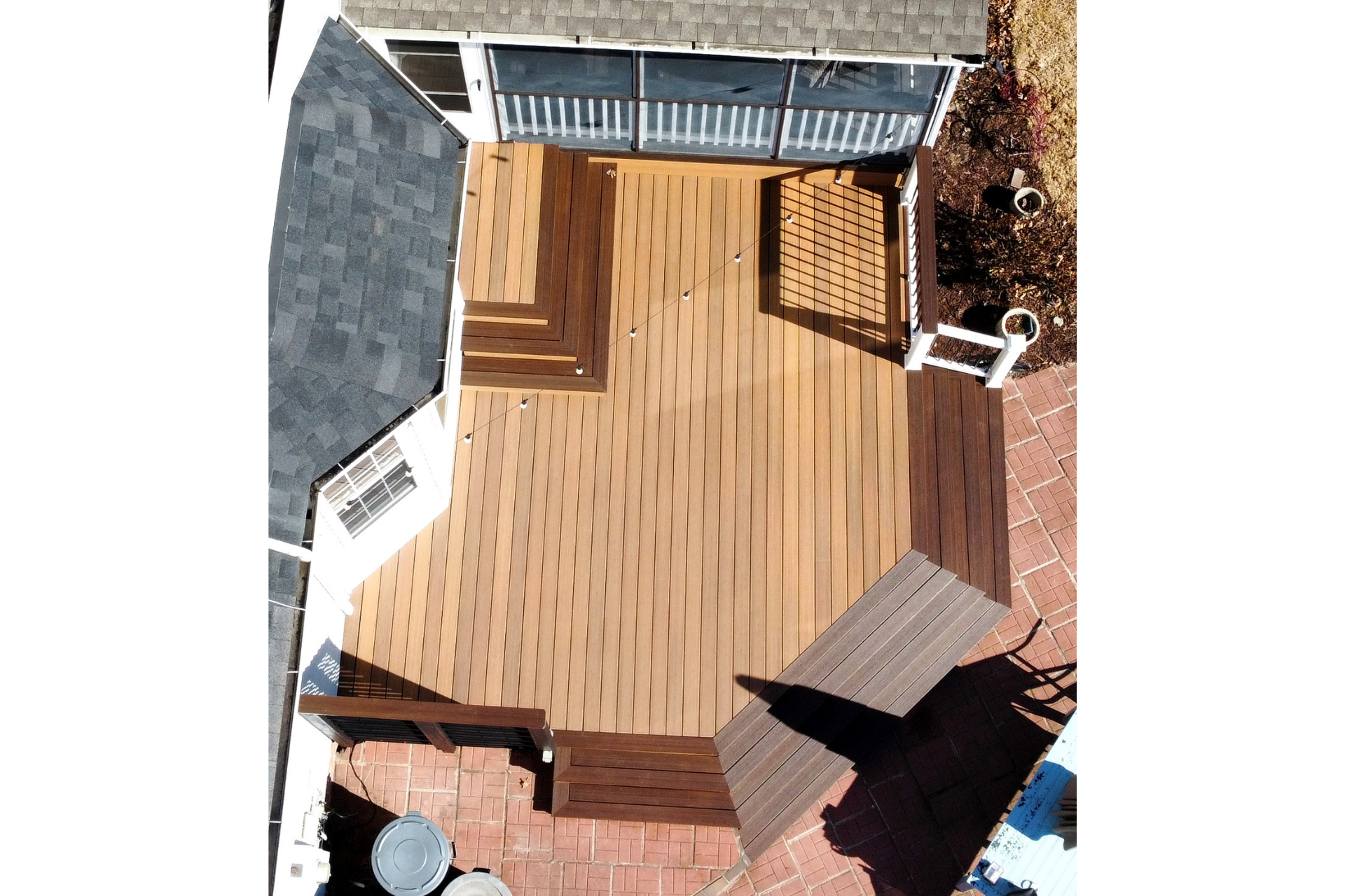 A bird’s-eye view of a light brown wooden deck attached to a house, featuring stairs, built-in benches, and a patio area.