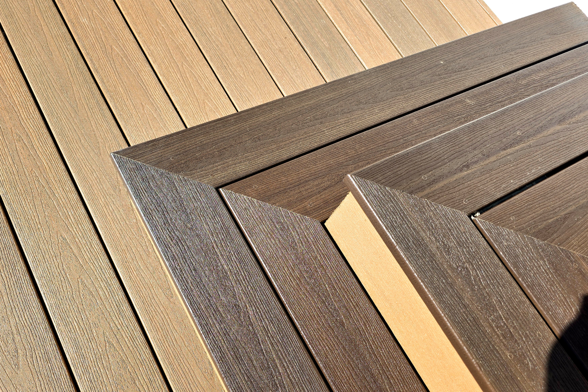 View of a deck featuring light tan planks bordered by dark brown composite trim pieces meeting at mitered joints.