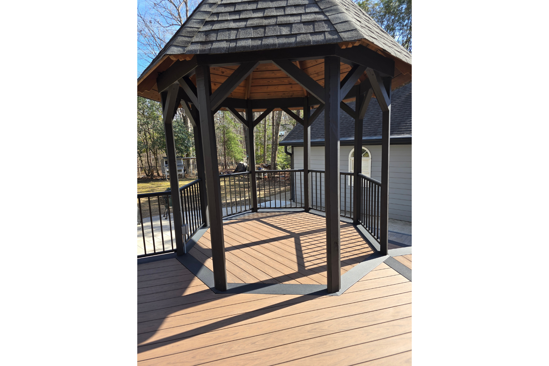 An outdoor gazebo with a shingled roof and dark wooden posts, situated on a wooden deck.