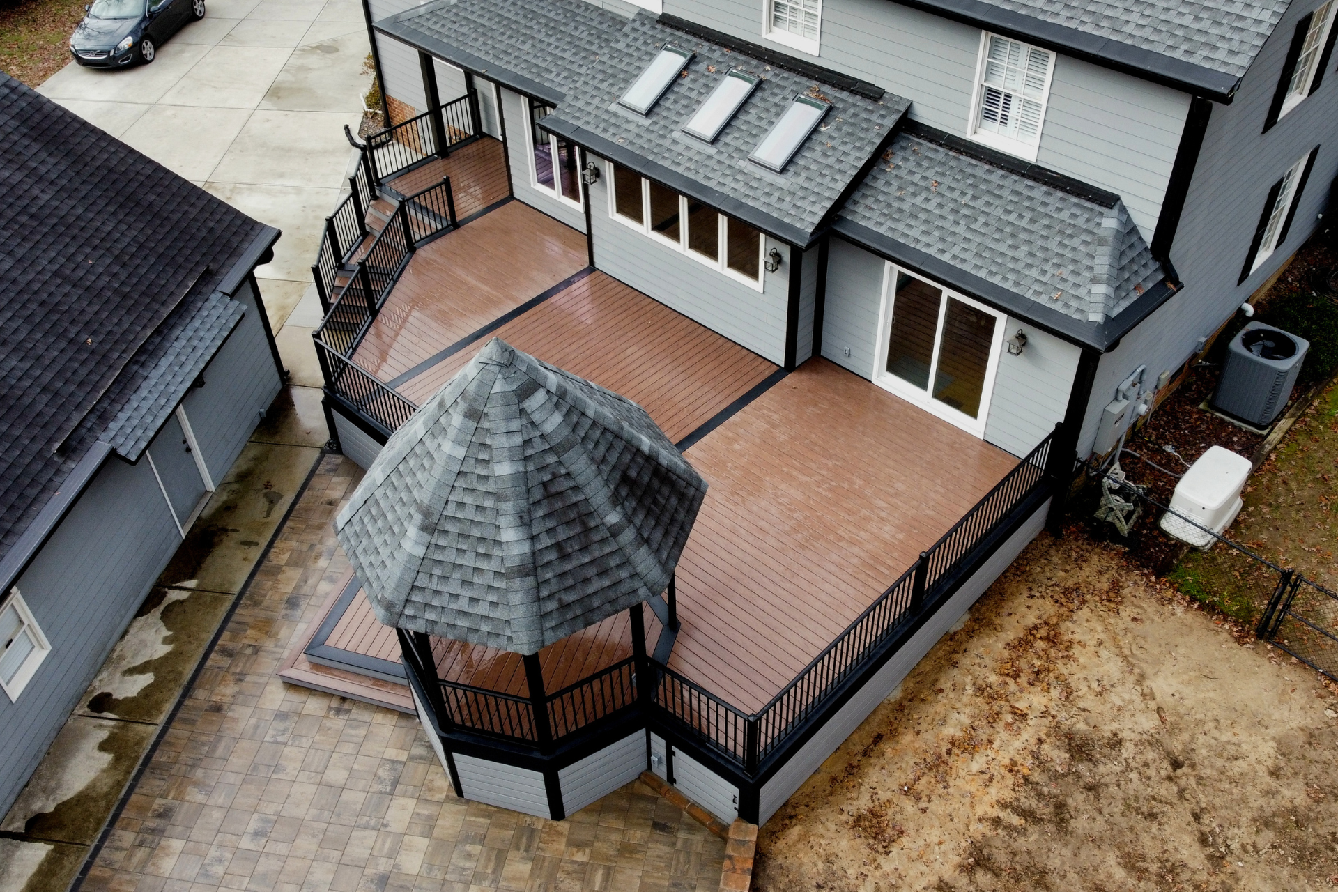 An aerial view of a multi-level composite deck attached to a gray house, featuring a gazebo and dark metal railings.
