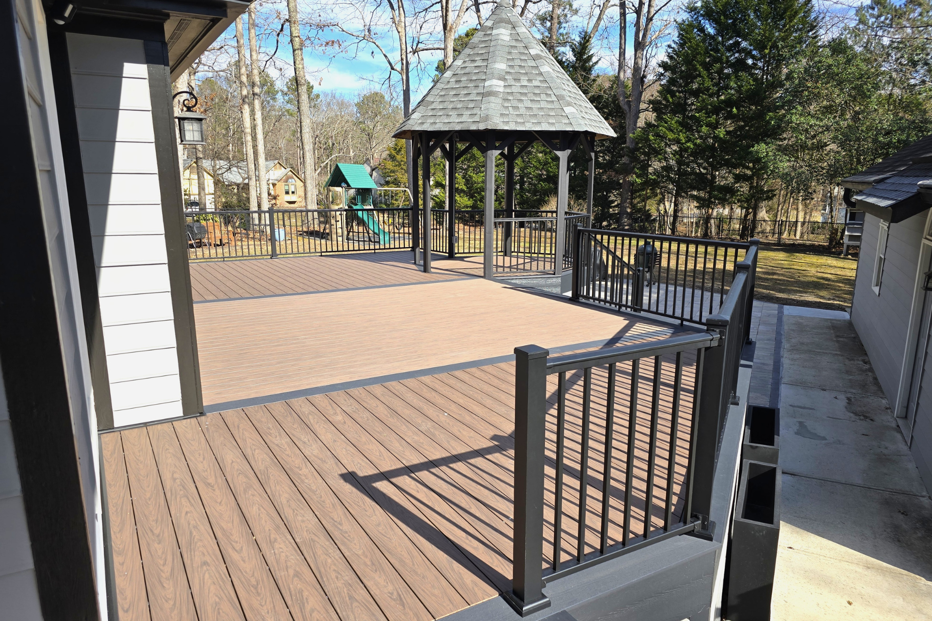 A multi-level outdoor deck with brown composite decking, black railings, and a gazebo, viewed from a patio level.