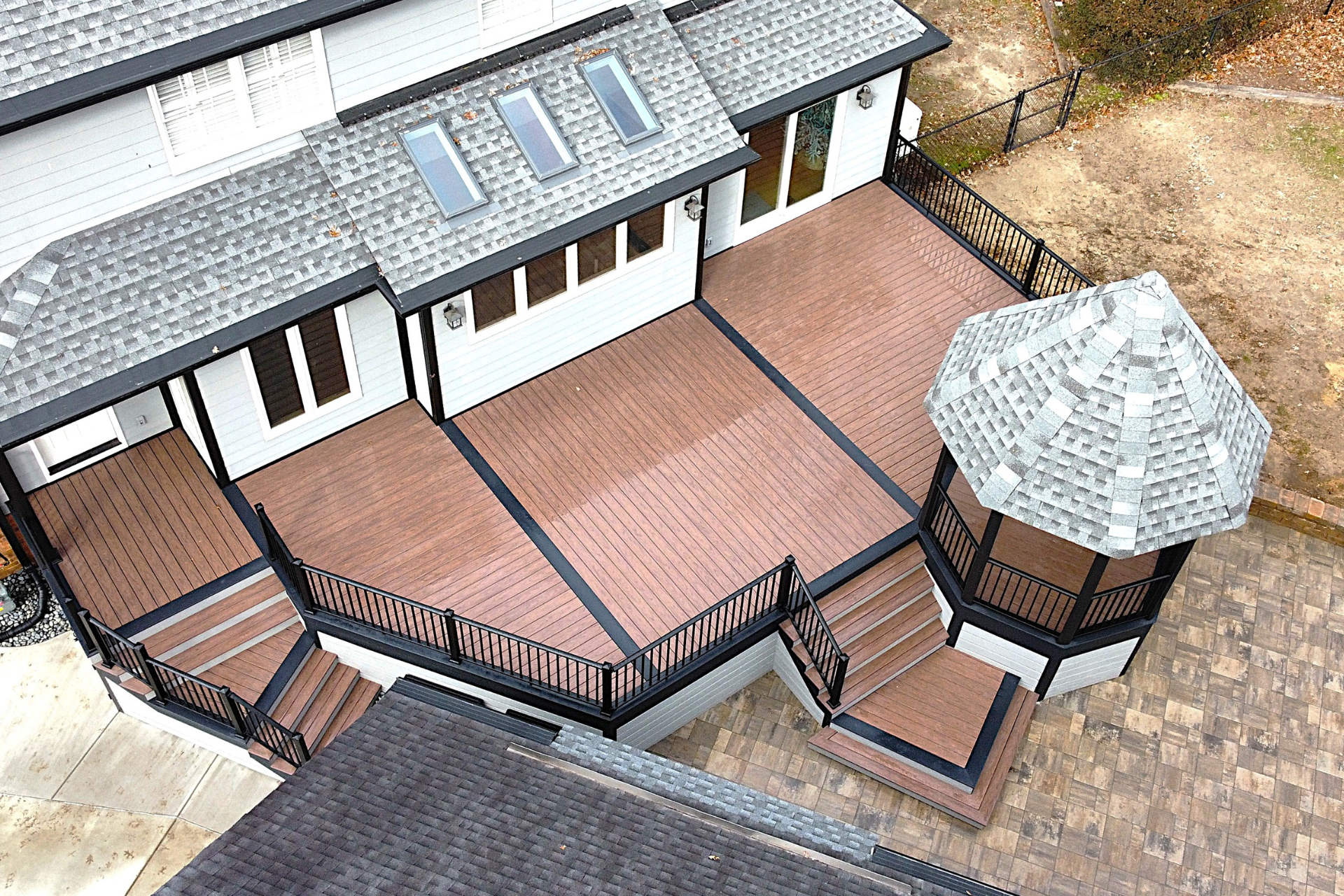 An elevated view of a house with a multi-level composite deck, black railings, stairs, and a matching gazebo.