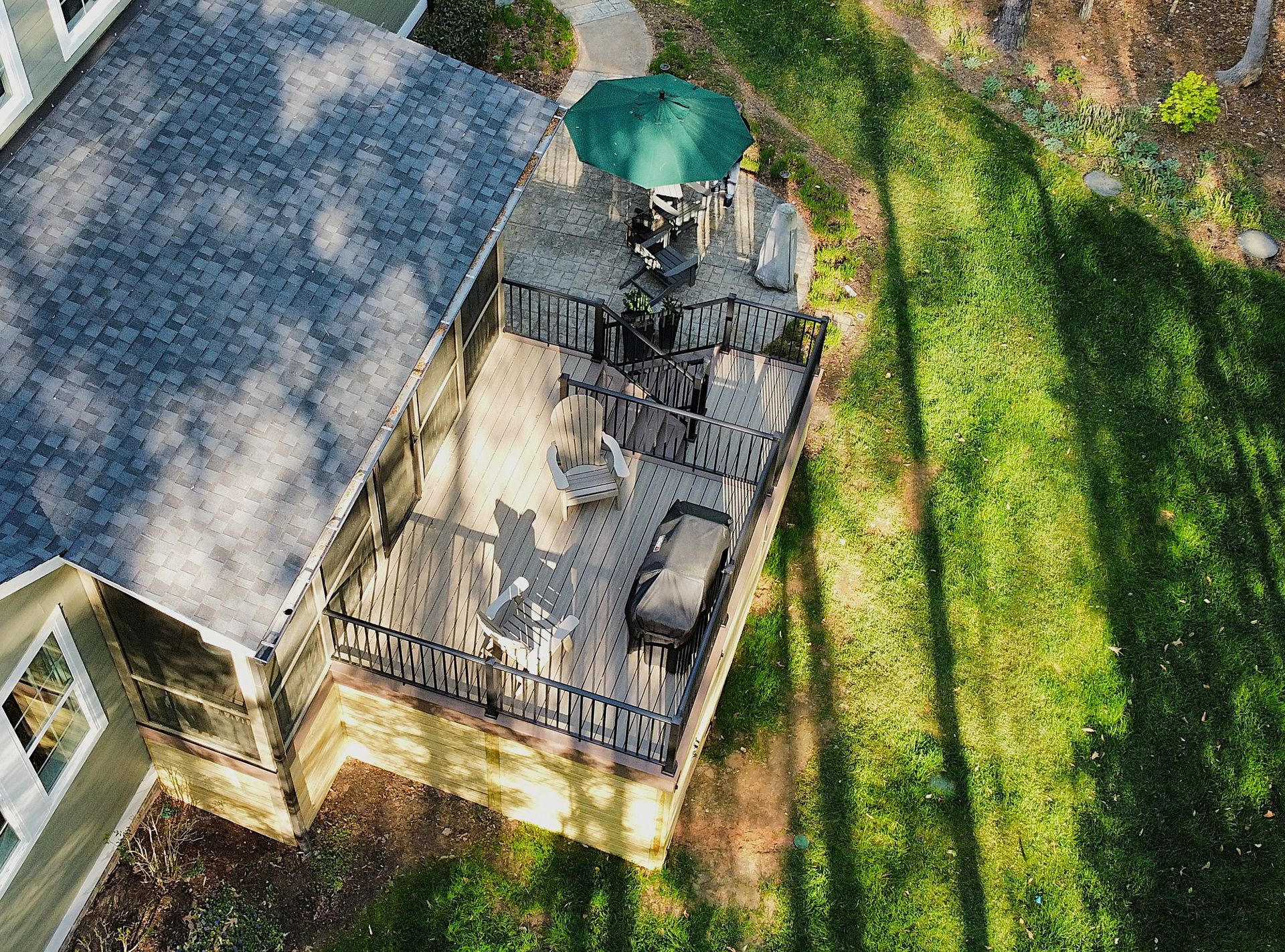 An overhead view of a house deck with patio furniture, a green umbrella, and black railings, overlooking a grassy yard.
