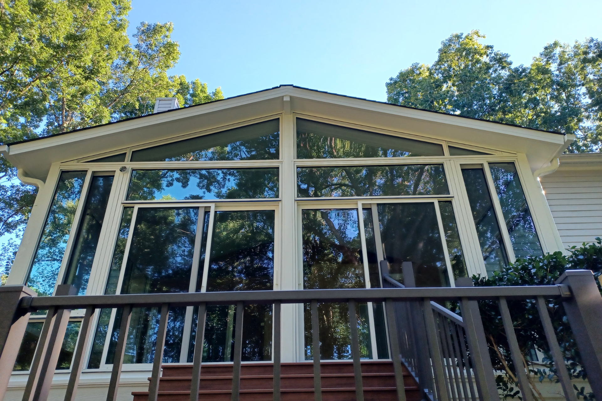 A low-angle view of a house addition featuring large glass sliding doors and windows under a gable roof, with a deck railing.
