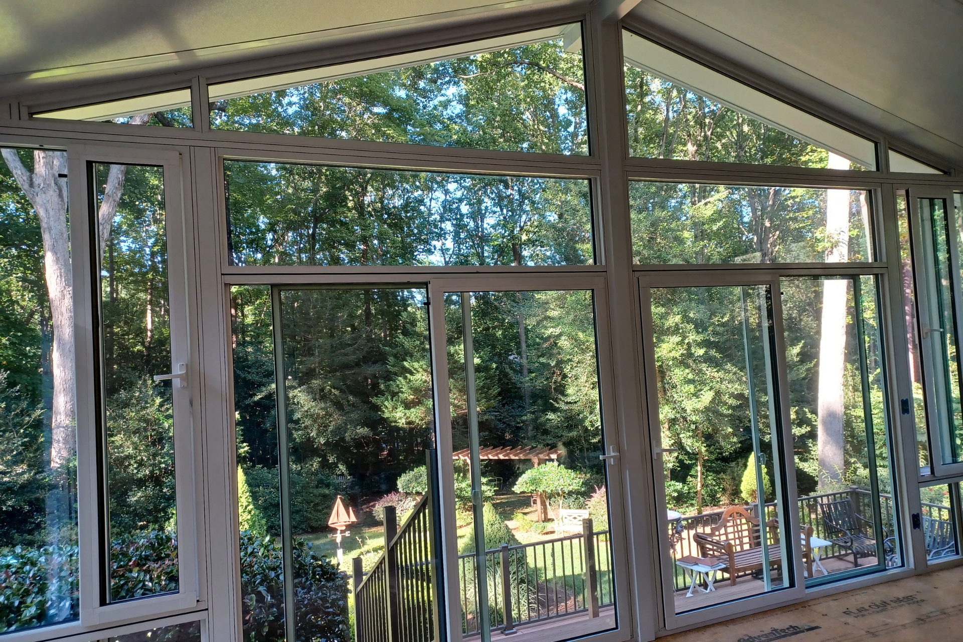 View of a lush backyard through large, paneled windows and a glass door inside a sunroom with a sloped ceiling.