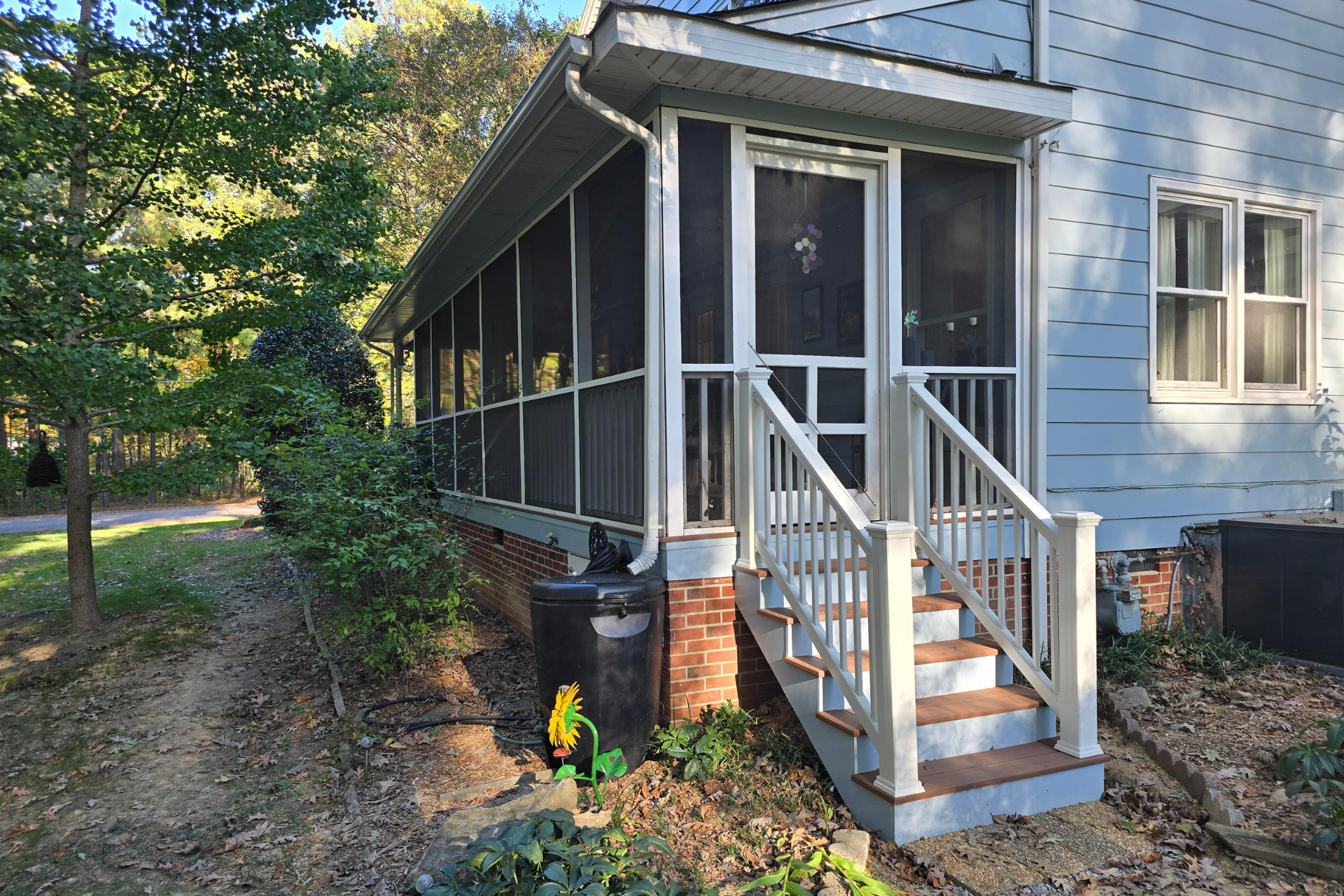 A blue house with a white-trimmed screened-in porch and steps leading up to a door, surrounded by trees and foliage.