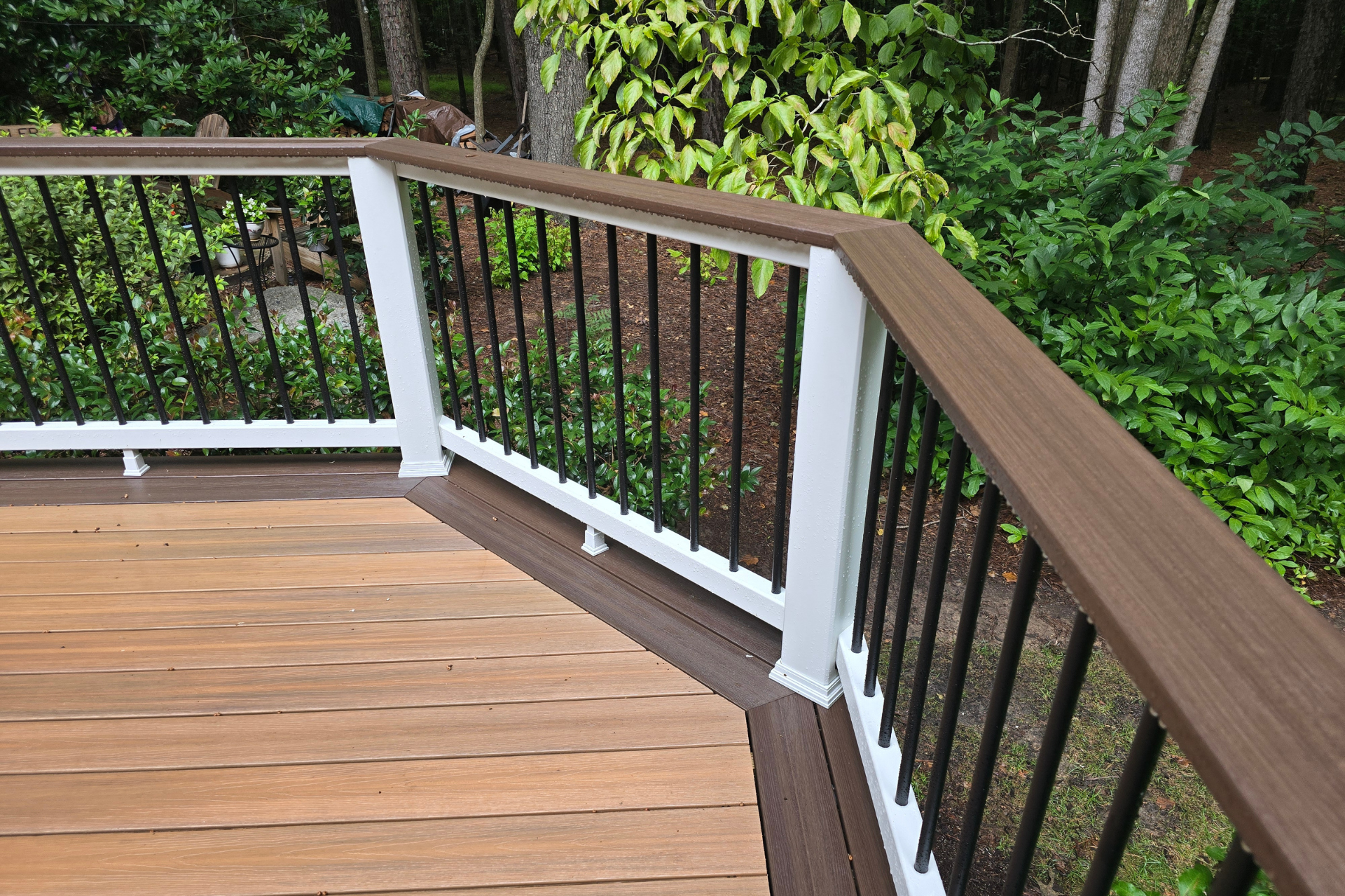 A corner of a wooden deck featuring white posts, dark brown railings, and thin black vertical balusters.
