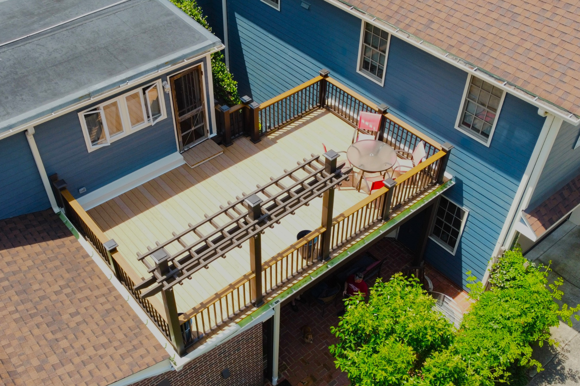 An elevated wooden deck with a pergola, seating, and railings attached to a blue house.