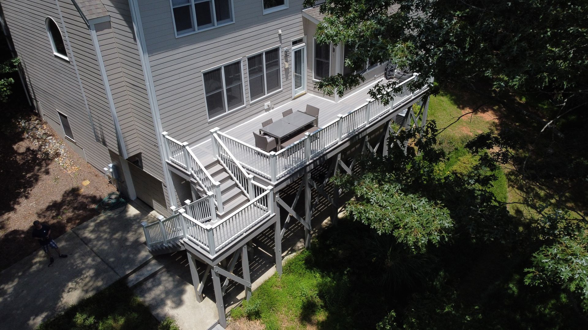 An elevated light gray wooden deck with white railings and stairs, attached to a house overlooking a wooded backyard.
