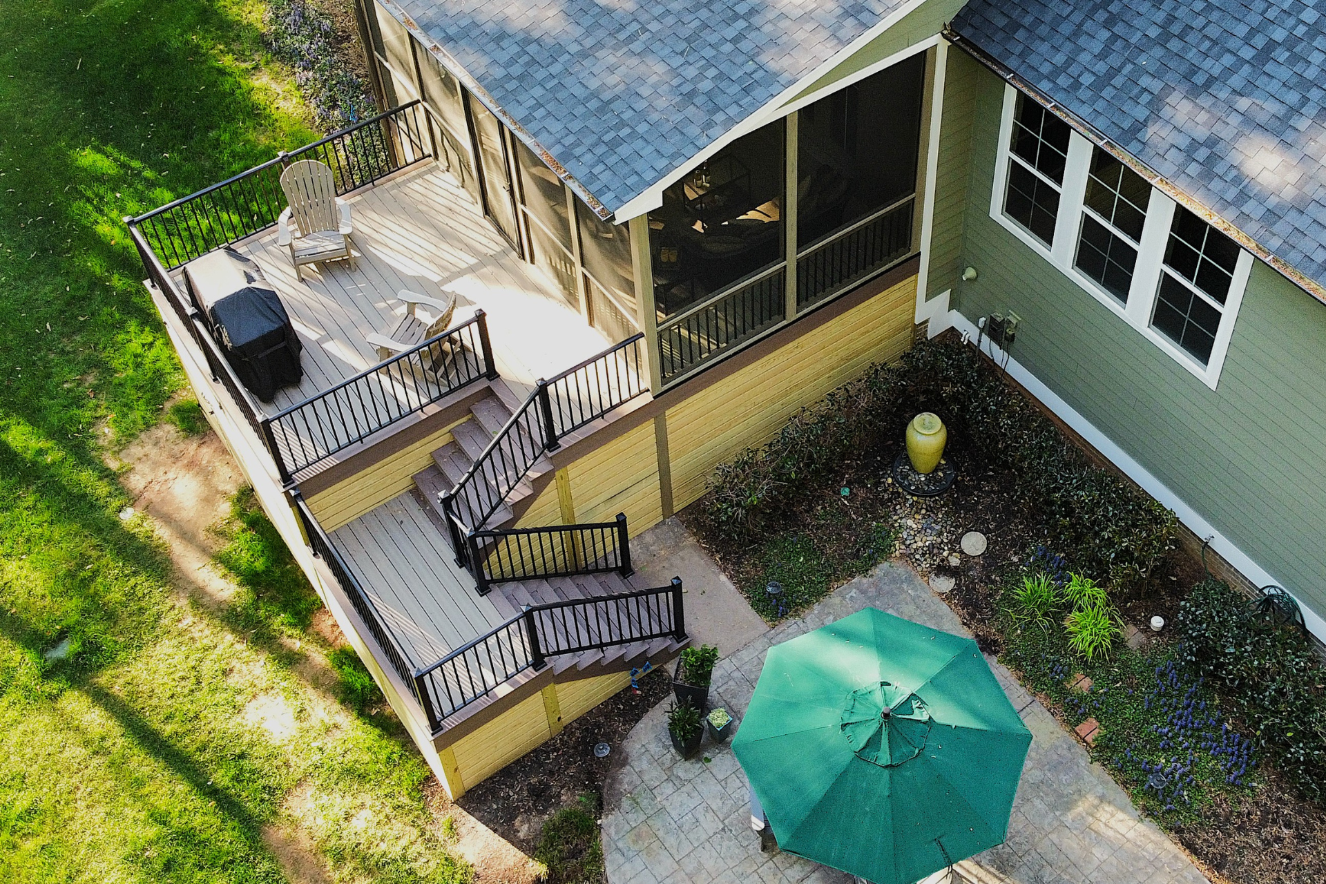 An aerial view of a house with a green exterior, a screened-in porch, a wooden deck, stairs, and a patio with an umbrella.