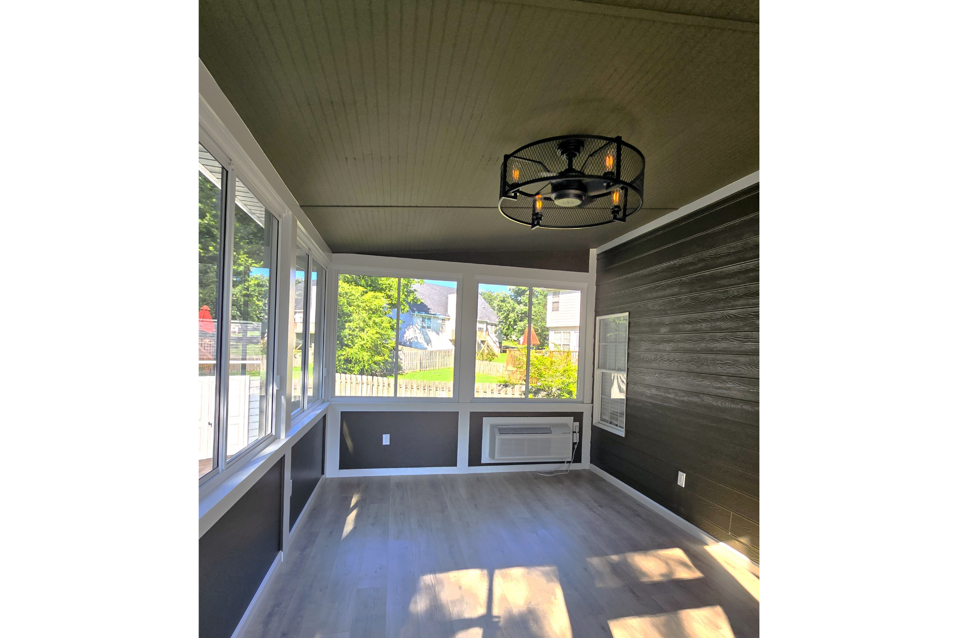 An empty sunroom with dark grey walls, light wood-look flooring, large windows, and a modern industrial ceiling light.