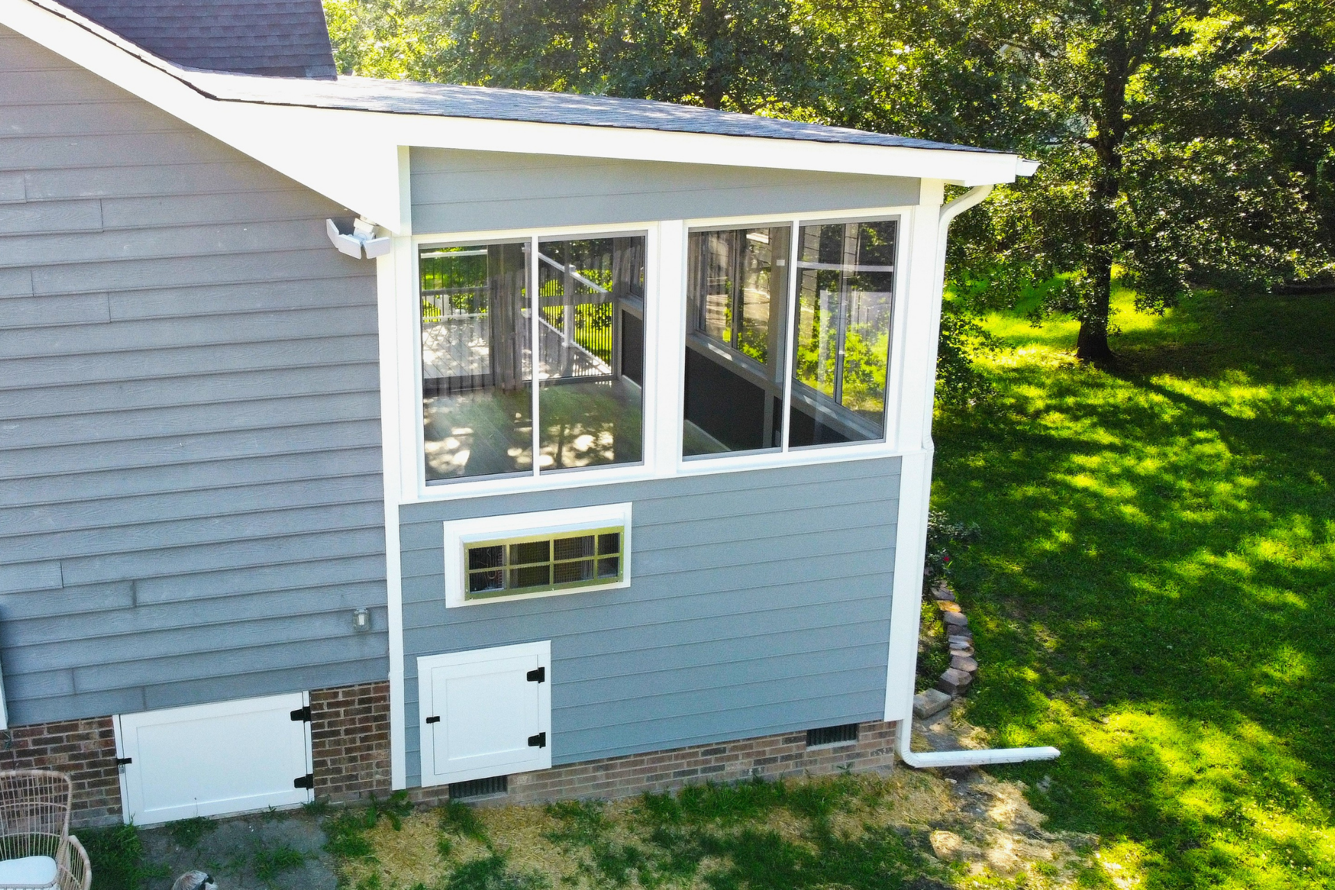 An elevated view of a gray house exterior featuring a screened-in porch with windows and two white basement-level doors.